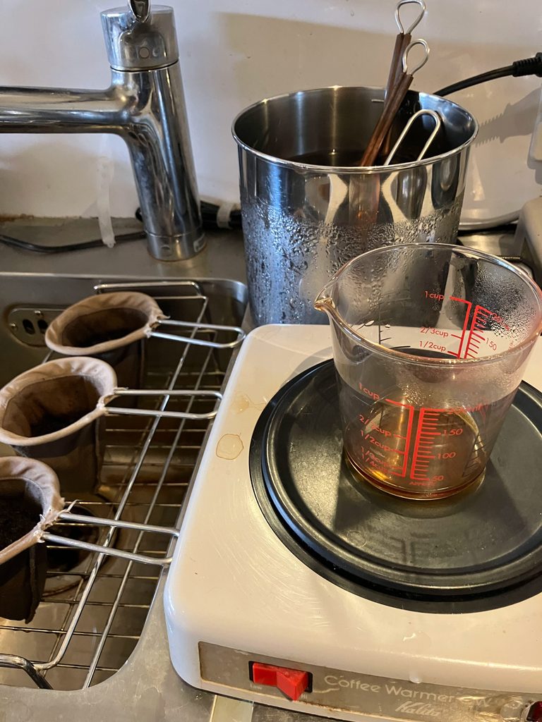 抽出したコーヒーをウォーマーで保温する喫茶店の厨房。奥のラックにネルフィルターが並ぶ